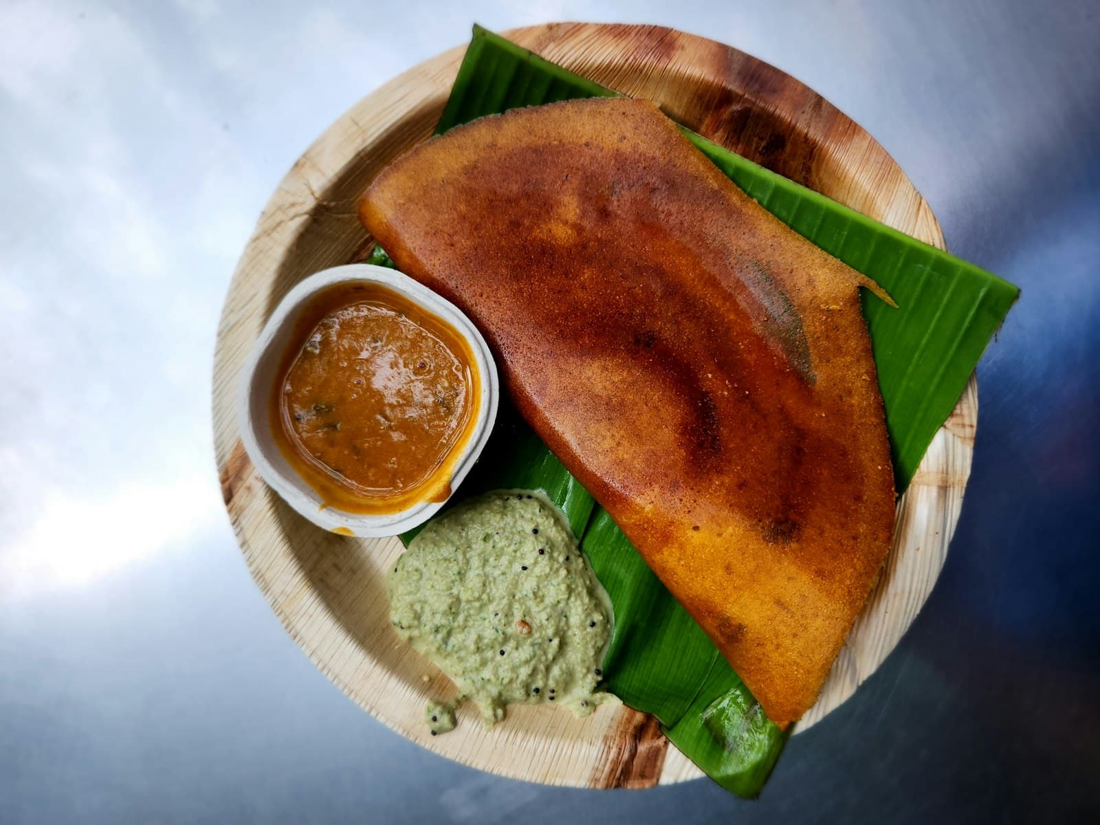 A rolled dosa on a wooden plate with sambhar and chutney