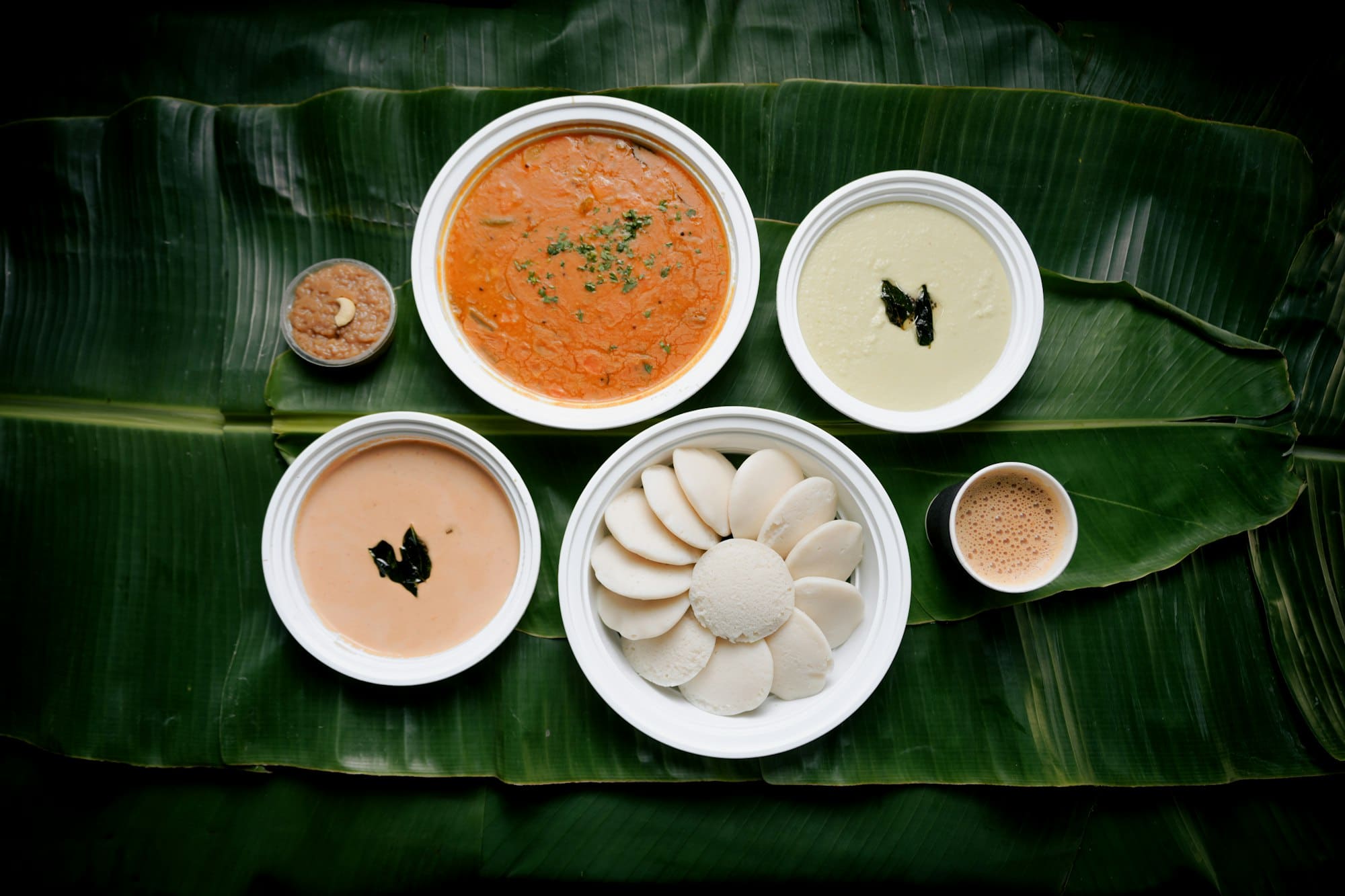 Steamed idlis on a banana leaf with chutneys and sambhar