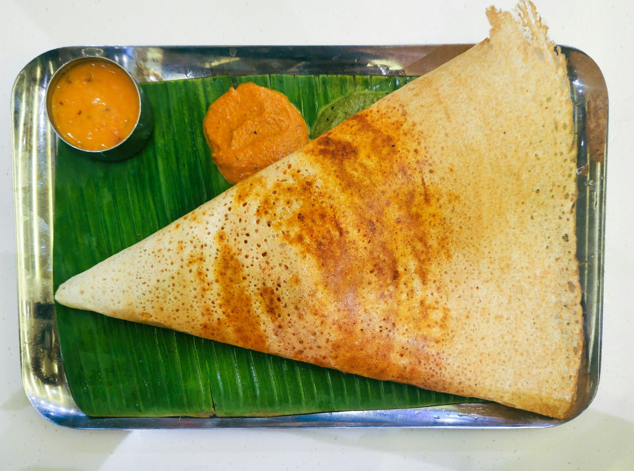 A crisp golden dosa folded on a banana leaf, served with coconut chutney and sambhar