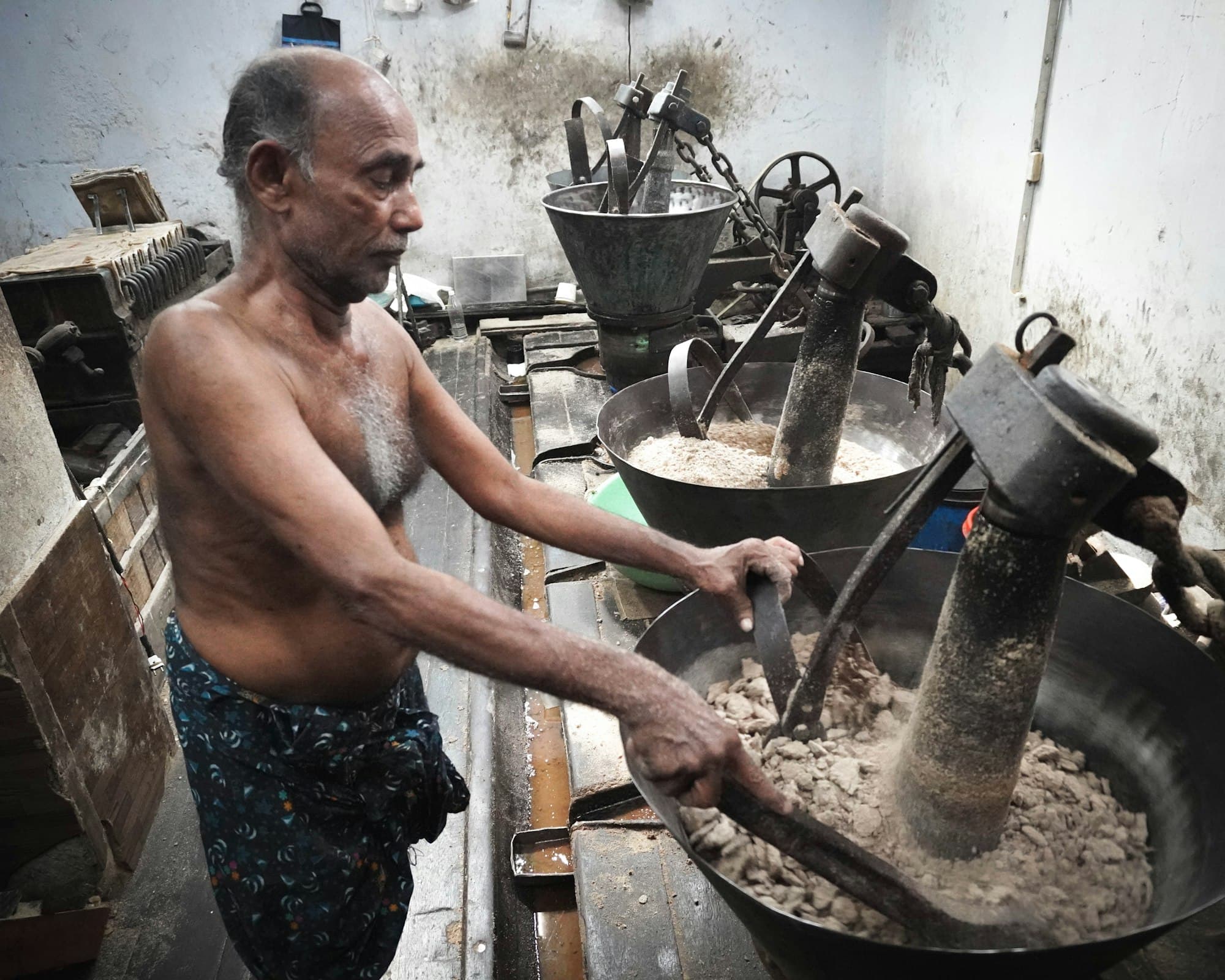 A cook working at a traditional stone grinder, preparing dosa batter